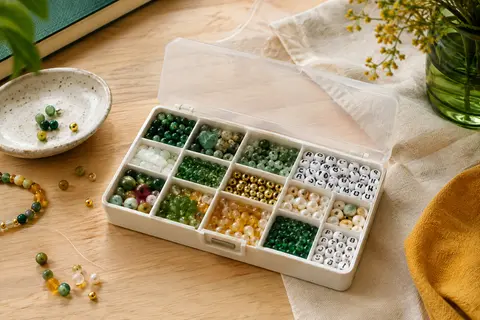 Perles vertes en pierre naturelle et lettres acryliques rangées dans une boîte compartimentée.